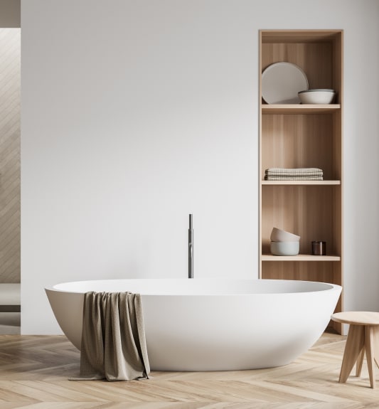 Baignoire îlot moderne : design minimaliste et ambiance spa. Baignoire îlot blanche, robinetterie minimaliste et parquet en bois clair à chevrons. Étagères intégrées décoratives dans la salle de bain moderne.