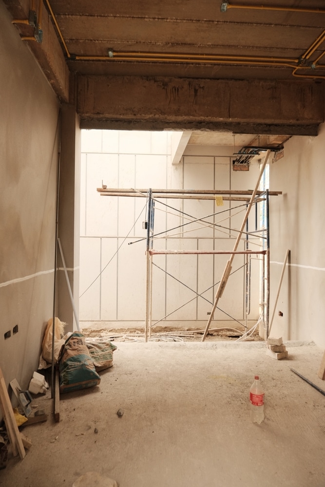 Chantier de construction : intérieur brut, béton et échafaudage. Intérieur de construction brut. Poutre en béton armé, conduits électriques jaunes et échafaudage central. Sacs de mortier sur le sol poussiéreux.