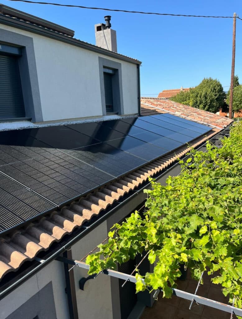 Installation de panneaux solaires sur toit en tuiles Panneaux solaires photovoltaïques noirs sur une toiture en tuiles romanes à côté d'une vigne verdoyante sous ciel bleu.
