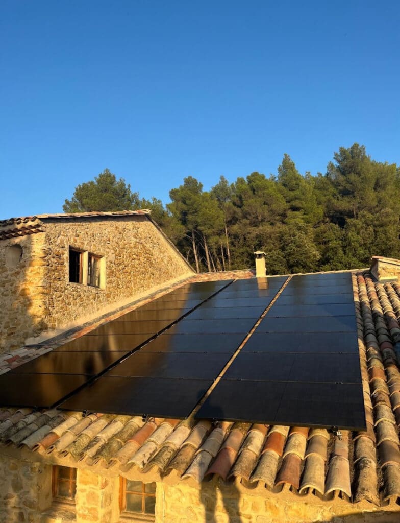 Panneaux Solaires sur Toit en Tuiles d'une Maison en Pierre Panneaux solaires photovoltaïques noirs sur le toit en tuiles d'une maison ancienne en pierre sous un ciel bleu.